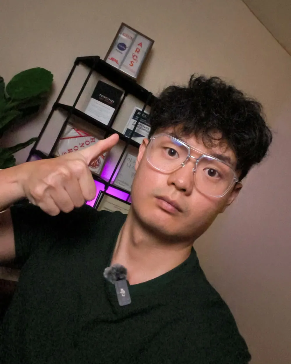 Patrick at his desk, pointing at a shelf of framed certificates behind him